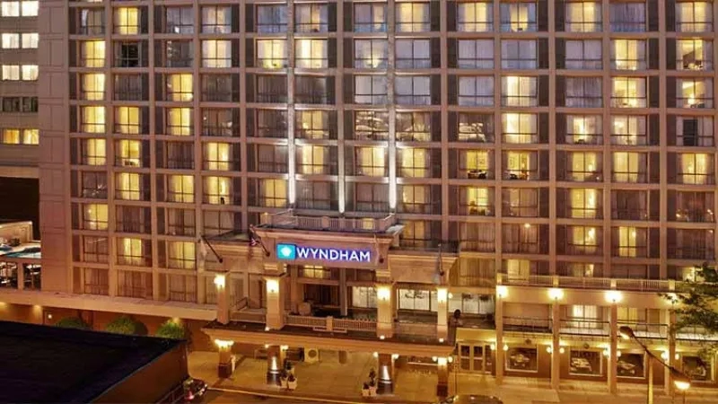 Exterior of Wyndham Boston Hotel at night with lights on the windows and a tree on the right side.