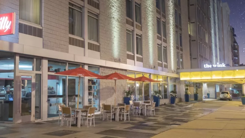 The Wink hotel exterior at night with a restaurant and tables outside with open umbrellas.