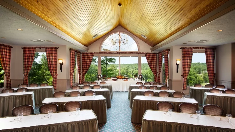 Woodloch resort's meeting room has tables, chairs, and a chandelier with large windows showcasing lush landscapes.
