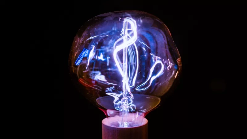 A glowing blue and white light bulb with a spiral filament on a wooden base.