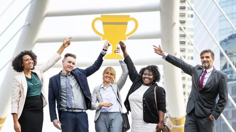 Group of people raising their hands, with a trophy icon above them, showing a cheerful and successful atmosphere.