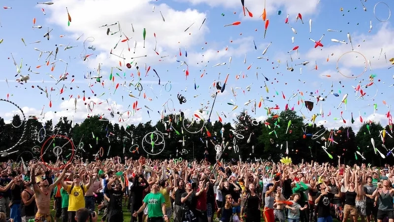 A large group of people are outside, and there are a lot of juggling balls flying around.