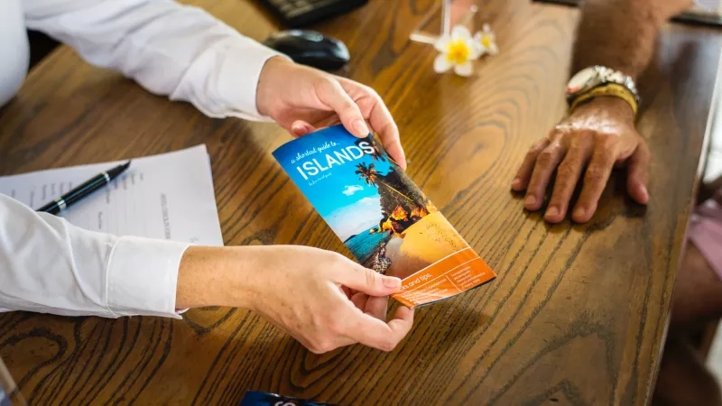 A person is holding an island brochure while sitting at a desk with another person.