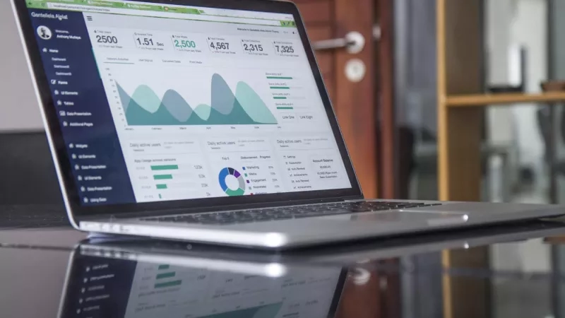 Laptop screen showing analytics with a pie chart and bar graphs on a glass table in an office.
