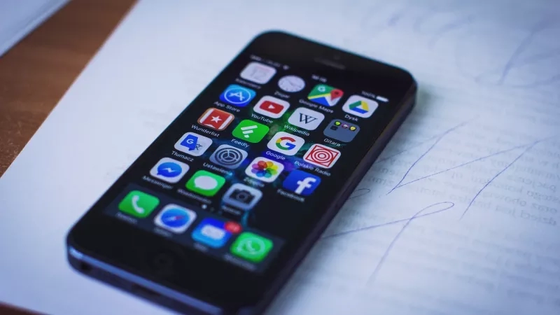 An iPhone with many apps on the screen on top of a piece of paper.