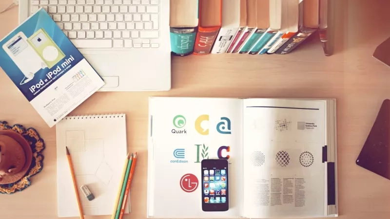 A desk with a book, laptop, cell phone, pencils, and other office supplies.