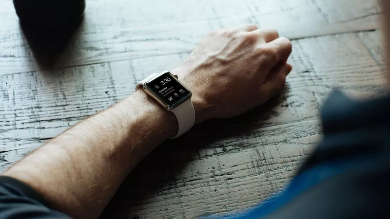 Apple watch on wrist with face showing time, calendar, and weather in blue and white tones.