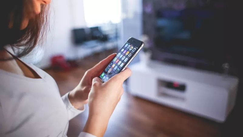 A woman is standing in front of a TV and holding a smartphone in both hands.