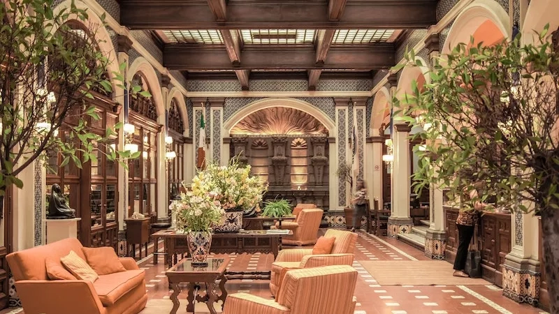The lobby of The Royal Sonesta New Orleans with beige furniture, potted plants, and a warm ambiance.