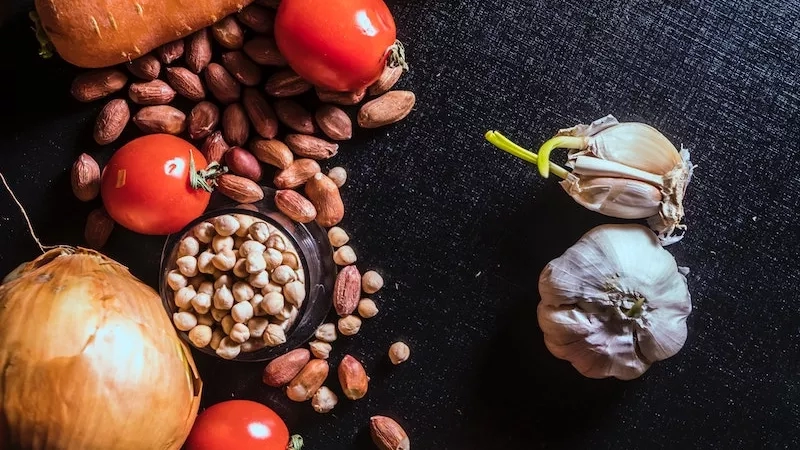 Different vegetables like onion, carrot, tomatoes, and chickpeas on a black background with a few peeled garlic cloves.
