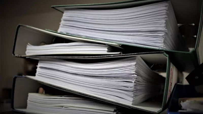 Three green binders with white papers on top of each other on a black table
