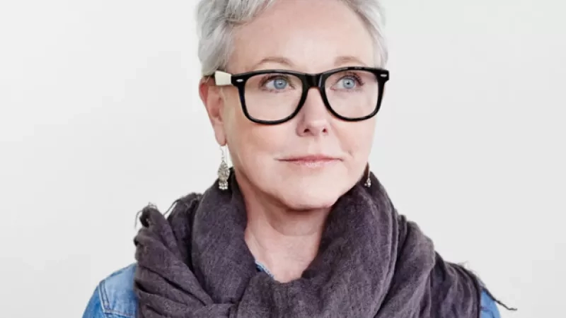 A portrait of a woman wearing glasses, a denim jacket, and a scarf around her neck.