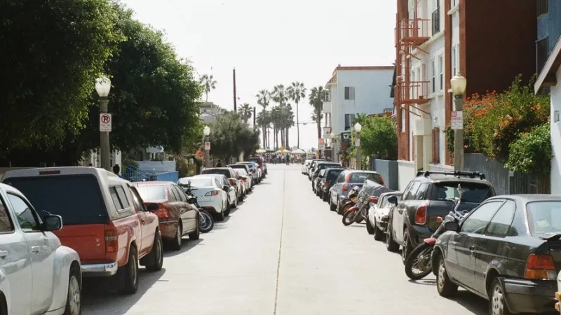 A long street with cars parked on both sides of the road with streetlights and buildings on the sides.