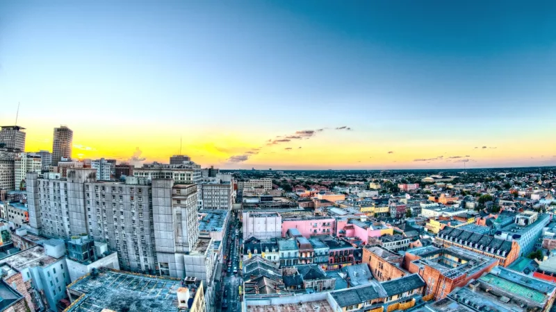 Aerial view of New Orleans skyline at sunset, showcasing diverse architecture and urban landscape under a vibrant sky.