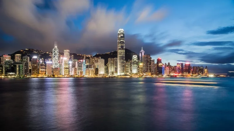 Hong Kong's skyline at night, with colorful lights reflecting in the water and mountains in the distance.