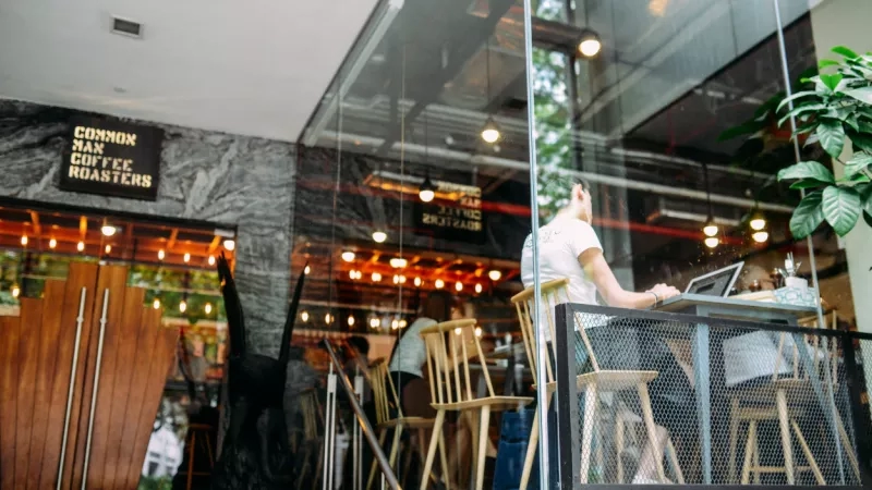 People sit at a table in front of a glass wall at the Common Man Coffee Roasters shop.