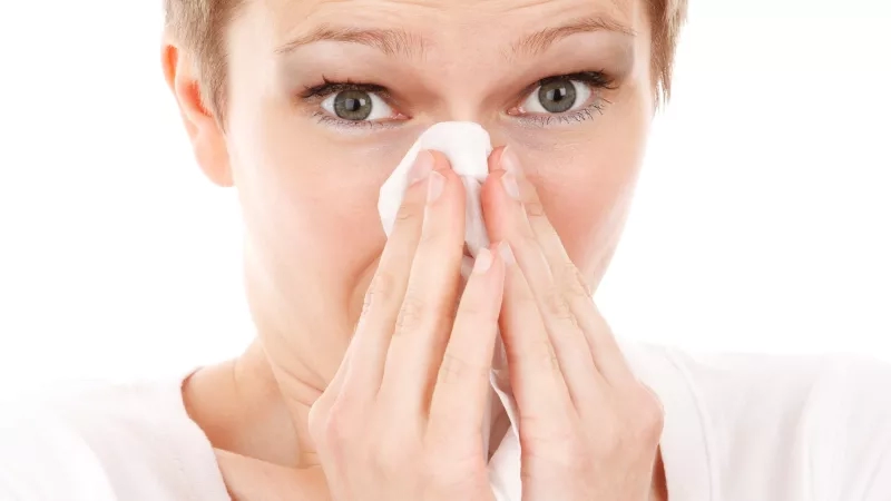 A woman blowing her nose into a handkerchief, experiencing symptoms of the common cold.