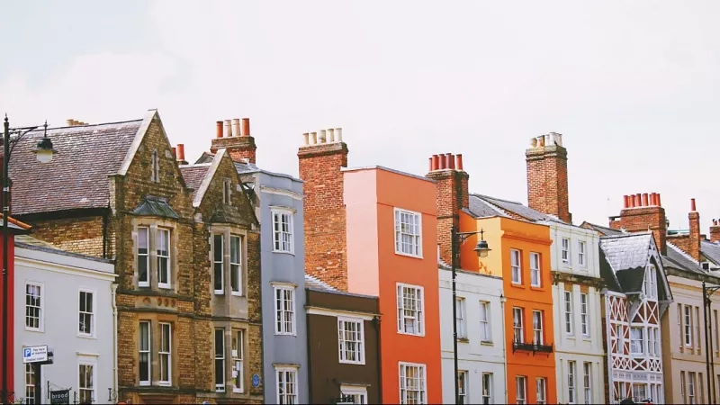 A row of colorful houses with chimneys and streetlights under a cloudy sky.