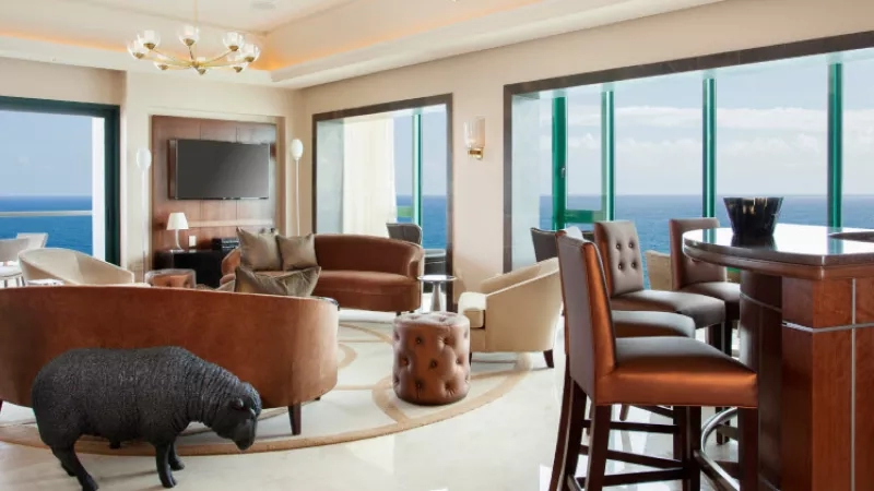A living room with a large window overlooking the ocean, with a sheep statue on the floor.