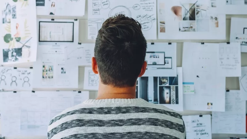 Man looking at a wall of paper with pictures, diagrams, and text related to architecture and landscaping.