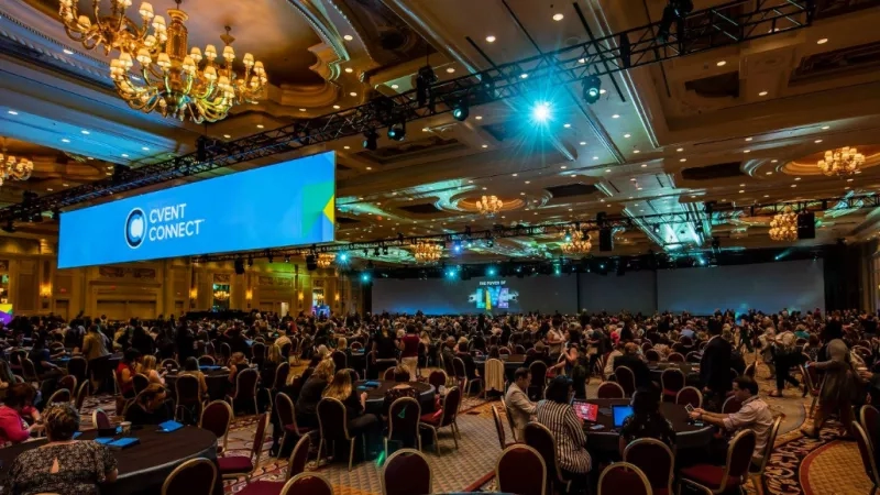 A large conference room with rows of chairs, a stage, and a big screen saying "EVENT CONNECT".