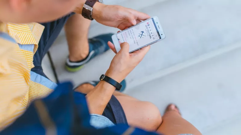 A man is sitting on stairs with a phone displaying content with the text 'off festival'.