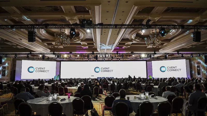 Cvent Connect Main Event Room with people seated at tables and large screens displaying Cvent Connect branding.