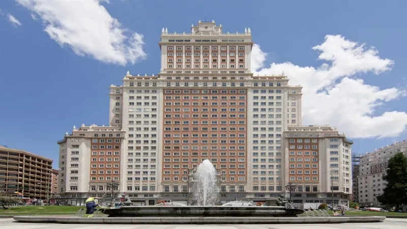 A beautiful Madrid hotel with a fountain in front of it on a sunny day.