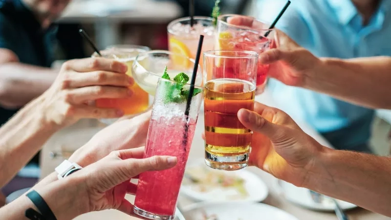 A group of people are gathered around a table with drinks and food, engaging in a social event.