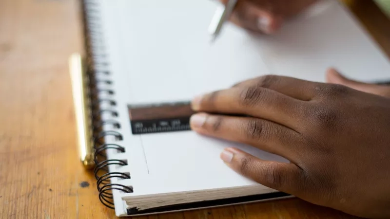 Person using a ruler to draw lines on a blank page of a spiral notebook.