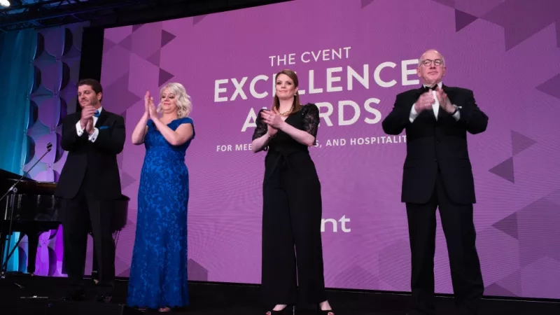 Four people are standing on stage in front of a purple background with The Cvent Excellence Awards written on it.