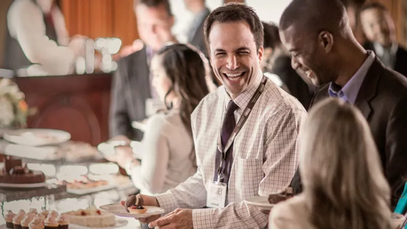 A man smiling while holding a plate of food at an event at the Omni King Edward Hotel.