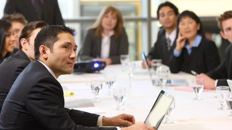 Group of business people having a meeting in front of a white table with laptops and glasses of water.