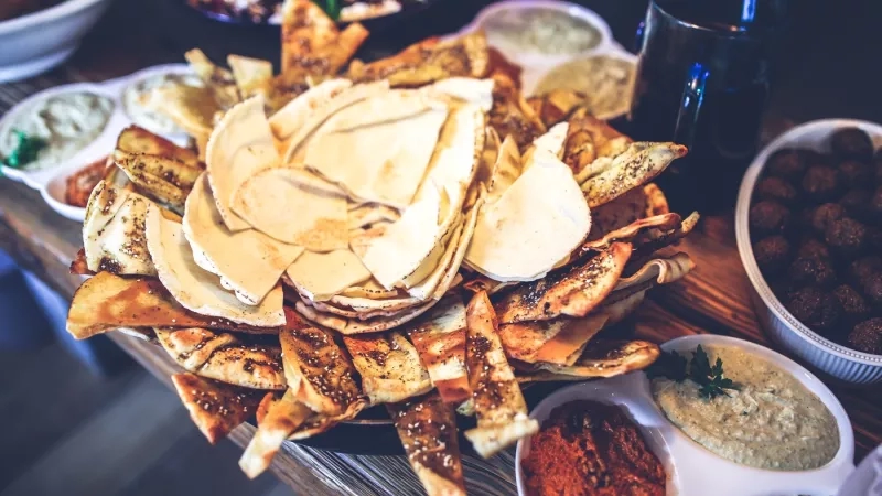 A plate of nachos with hummus and other dips on a wooden table, with a glass of water.