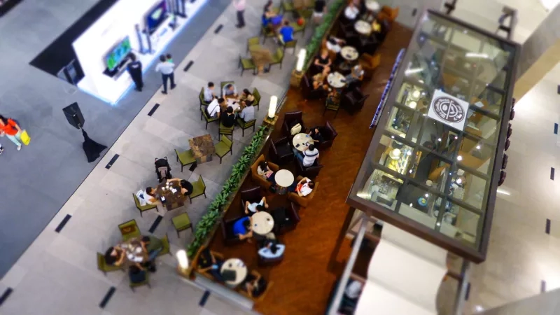 A bird's-eye view of the interior of a shopping mall with a cafe in the middle.