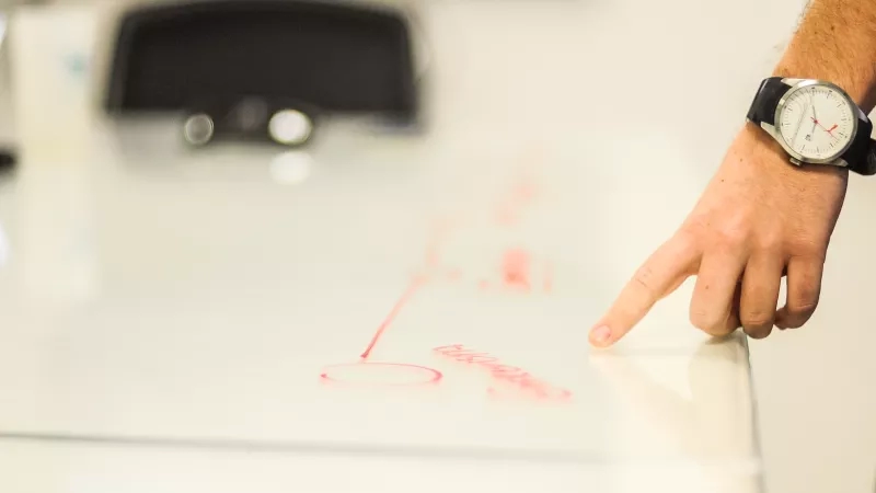 A person pointing at a glass table with red text on it and a watch on their wrist.