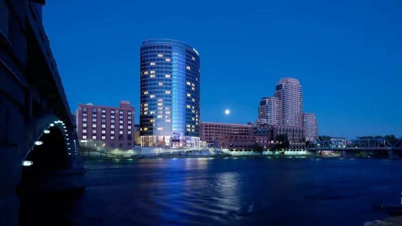 The Westin Grand Rapids building at night with a bridge in the foreground and river.