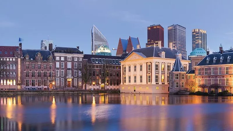 The Hague's skyline with buildings, trees, and a body of water reflecting the lights at dusk.