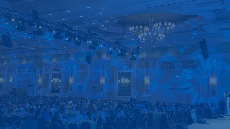 A large conference room with a speaker on the stage in front of a large audience.