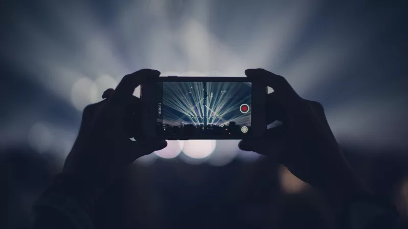 A person is recording a concert on their phone with the red record button showing.