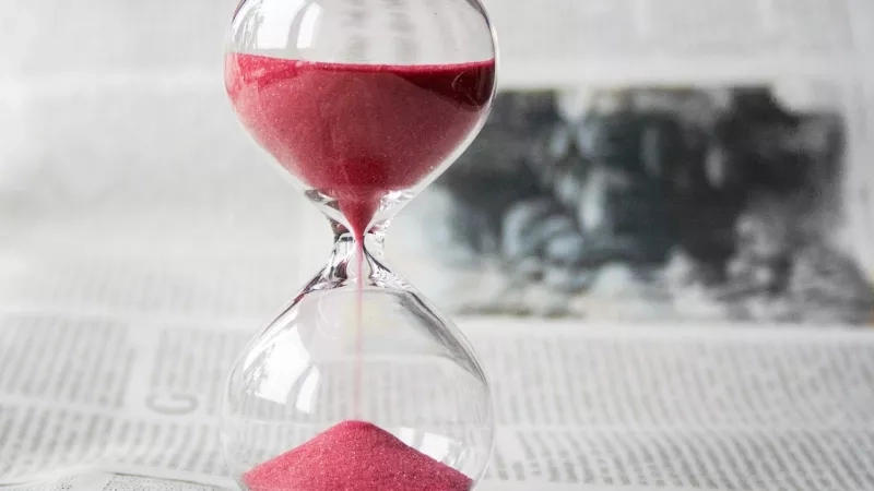 Hourglass filled with pink sand on top of a newspaper with a blurred background.