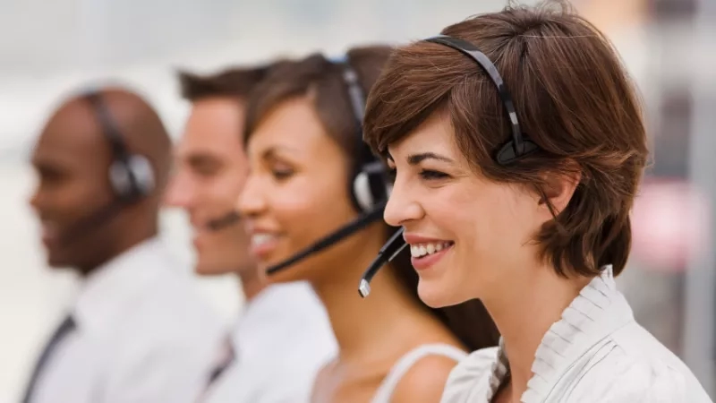 Portrait of call center team with headset smiling in the office with copy space on background.