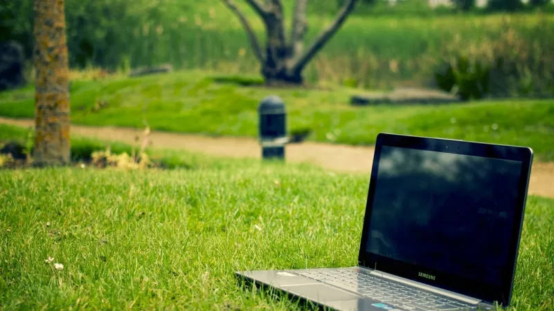 Samsung laptop is placed on the grass, with a pathway and trees in the background.