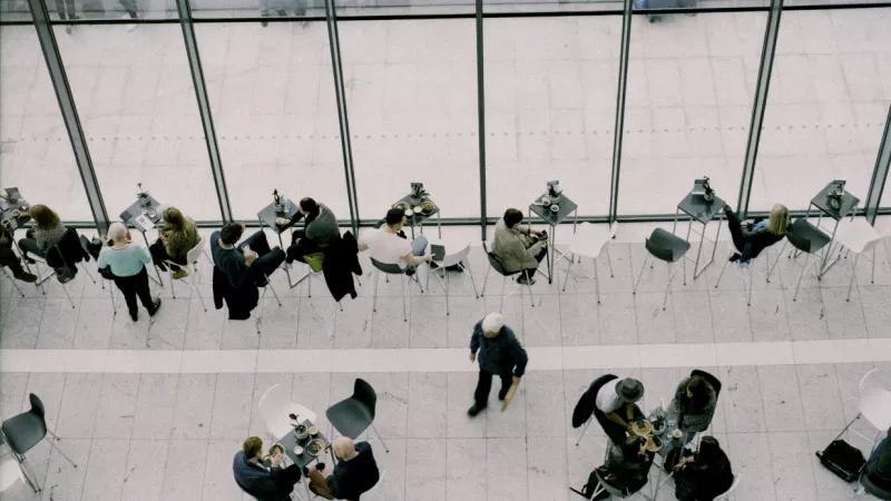 An aerial view of the lobby, which has a glass wall and many people seated at the tables.
