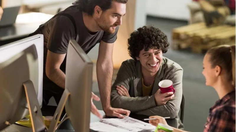 A group of three people laughing and working together in an office, discussing a project.