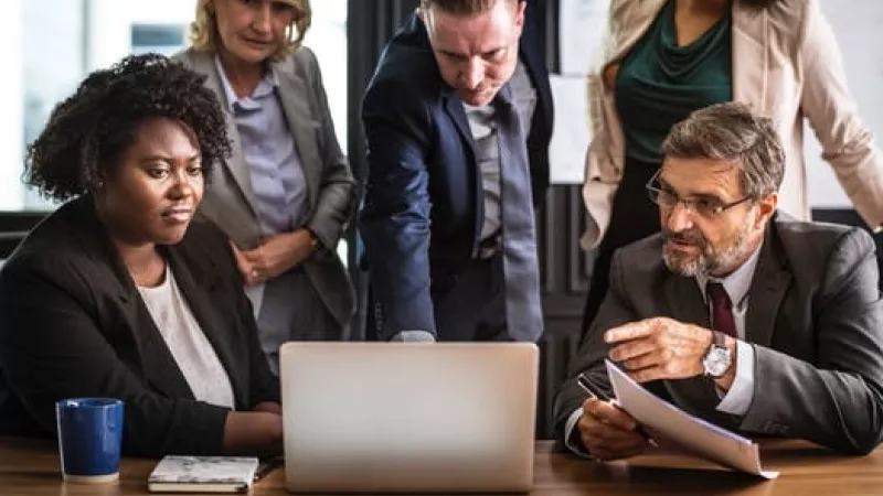 Group of business people sitting around a table in a meeting at the office with a laptop.