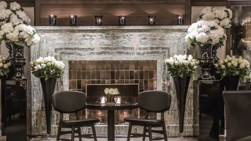 May Fair Hotel lobby with white flowers and chairs in front of a fireplace.
