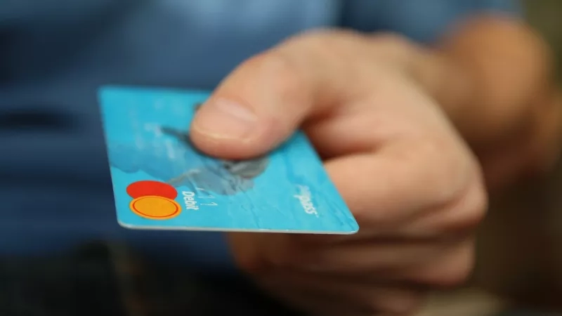A hand holding a credit card with a blue background and the word debit on the front of it.