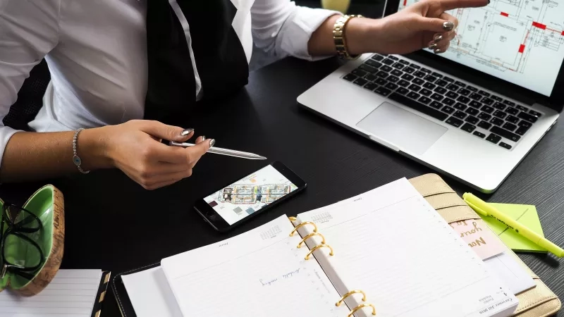 A woman using her laptop and cell phone to review floor plans for her property.