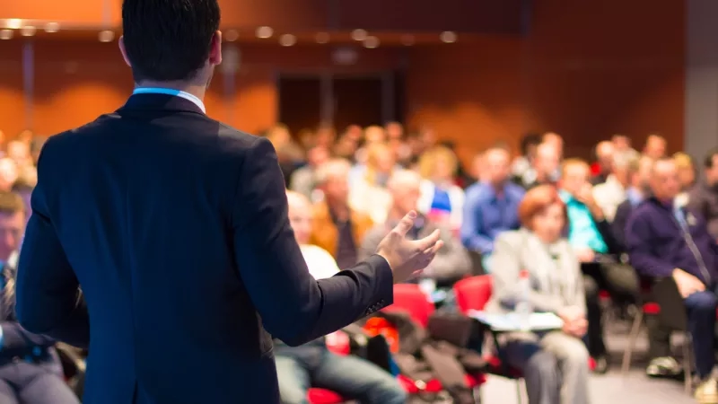 A man is speaking at an event in front of a large group of people.